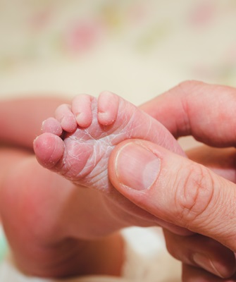 Small children's leg in dad's strong male hands. Tenderness and love from birth. Care and raising of children health. Happy Family concept.